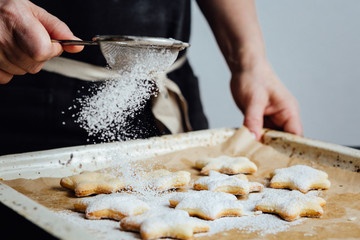 Hands of cook adding powdered sugar to cookies as a topping
