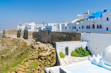 Blue and white washed buildings and ancient city wall at rocky coast of the town Asilah, Morocco, North Africa