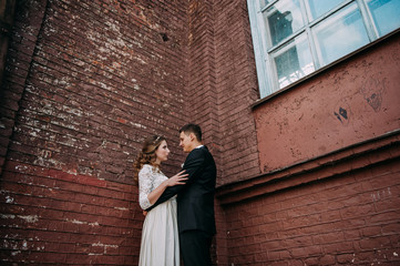 Fototapeta na wymiar Newlyweds embracing next to red brick wall. Young wedding couple.