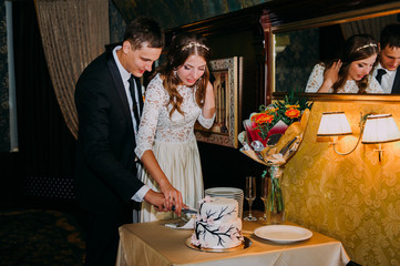 Stylish bride and groom in the restaurant cutting cake