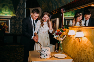 Stylish bride and groom in the restaurant cutting cake