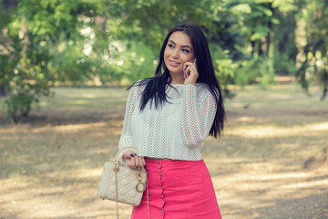 woman in white shirt standing in park, speaking on cell phone