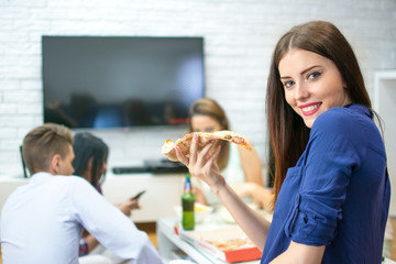 Young woman eating pizza while sitting with her friends at home.