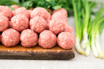 Raw meatballs on a rustic wooden cutting board on a stone backgr