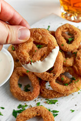Man Holding Fried Breaded Onion Rings with sauce. on white wooden board, background.