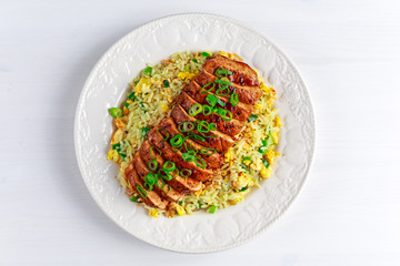 Chinese style Egg fried rice with sliced pork fillet on white wooden table.