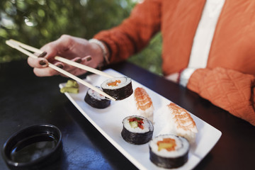 close up of a sushi plate with a female hand holding chopsticks