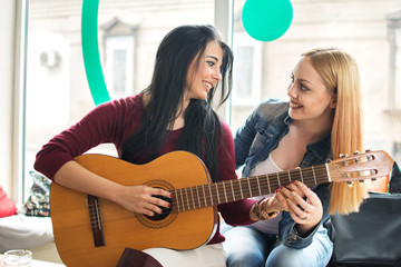 Girl teaching her friend to play guitar.