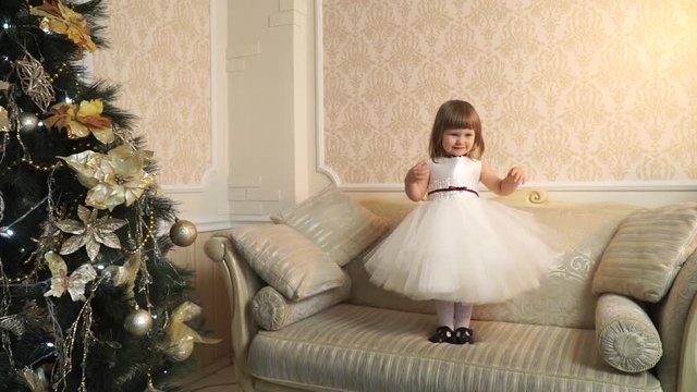 Little girl standing awkwardly on the couch and playing with dress