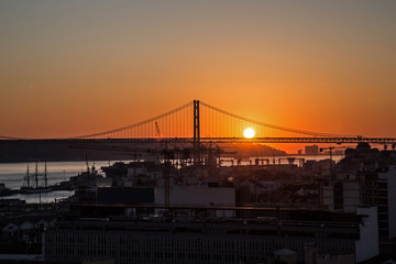 Sonnenuntergang hinter der Ponte 25 de Abril, die Brücke über den Tejo in Lissabon ( mit Industriehafen im Vordergrund)