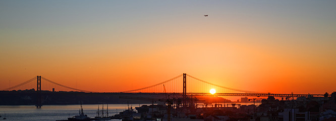 Obraz premium Sonnenuntergang hinter der Ponte 25 de Abril, die Brücke über den Tejo in Lissabon ( mit Industriehafen im Vordergrund)