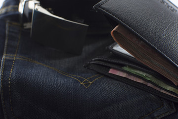 Dark jeans and black leather belt closeup holding a wallet with money.
