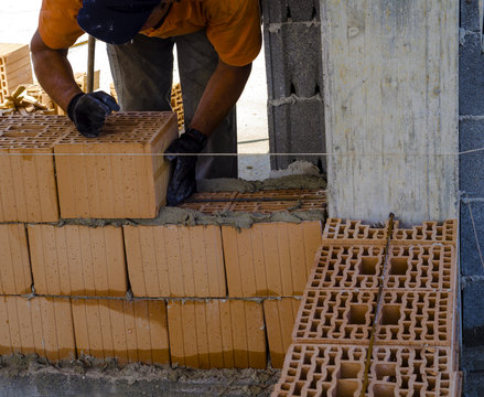 construction worker bricklayer installing red brick with trowel putty knife outdoors