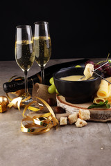 Gourmet Swiss fondue dinner on a winter evening with assorted cheeses on a board alongside a heated pot of cheese fondue with two forks dipping bread and white wine behind in a tavern or restaurant