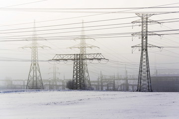 Electricity pylons from distribution power station in foggy winter freeze