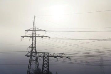 Electricity pylons from distribution power station in foggy winter freeze