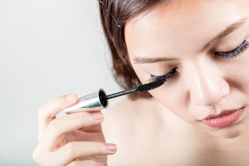 Woman applying black mascara on eyelashes with makeup brush