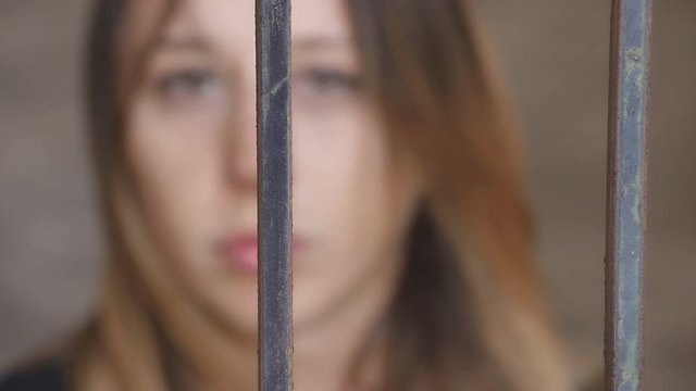 young woman behind bars while the wind moves the hair