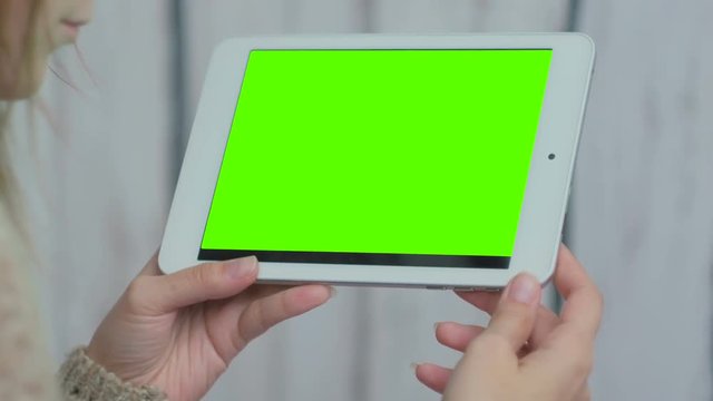 Woman looking at horizontal tablet computer with green screen. Close up shot of woman's hands with pad. White wooden background