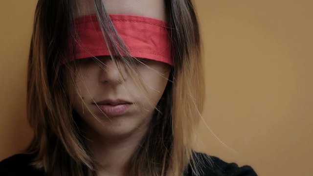 abused woman with eyes blindfolded with red ribbon