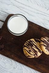 Glass of milk and stack of shortbread cookies with chocolate drizzle on a dark wooden board. White copy space. Minimal style food photography