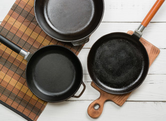 Several empty cast-iron frying pans on a white wooden background. View from above. Space for text.