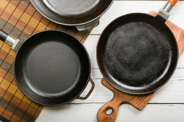 Several empty cast-iron frying pans on a white wooden background. View from above. Space for text.