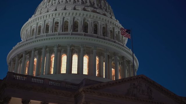 US Capitol building illuminated dome at night with American Flag.