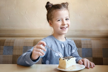 Fototapeta na wymiar Cute little girl eating tasty cake in kitchen