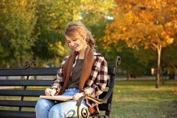 Fototapeta na wymiar Young female artist drawing sketch while sitting on bench in beautiful park