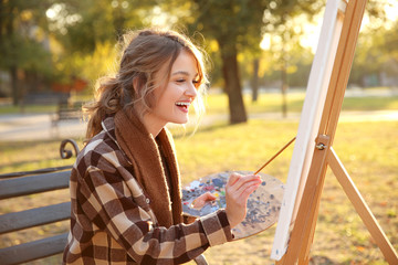 Young female artist painting picture in autumn park