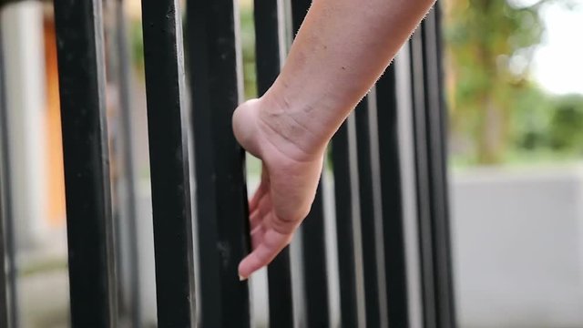  woman's hand gently touch the iron bars of a building