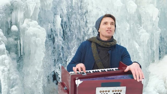 Happy young man playing the harmonium on a frozen waterfall