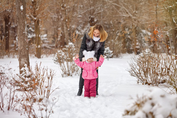 Fototapeta premium Mother and daughter walking on snow outdoors. Family walk in a winter park. Family happiness.