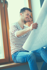 Young couple sitting on the floor and looking at the blueprint of new home