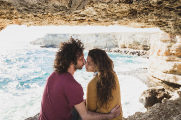 Couple enjoying together on rocky coast at sunset light