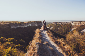Bride and groom walking in mountains at sunset. Around the stunning canyon