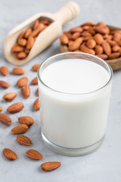Almond milk in glass with almonds on background, vertical