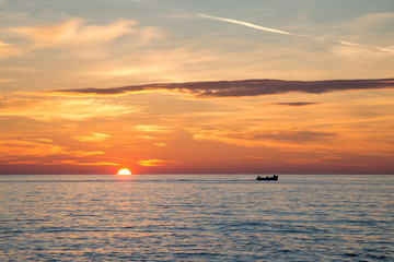 Fishing boat on the background of incredible golden sunrise, clouds and rising sun.