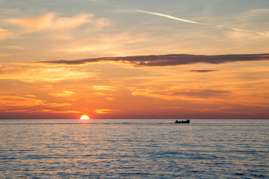 Fishing boat on the background of incredible golden sunrise, clouds and rising sun.