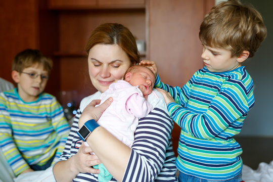 Mother holding newborn baby girl on arm with two kids boys