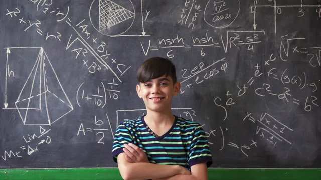 Concept on blackboard at school. Young people, student and pupil in classroom. Smart hispanic boy writing math formula on board during lesson. Portrait of male child smiling, looking at camera