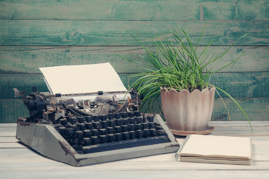 Dirty vintage typewriter with plant and blank notebook