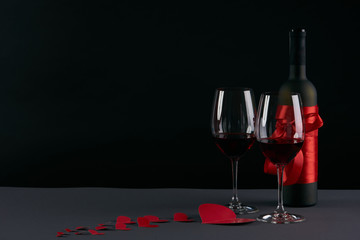 Wine bottle and two wineglasses with red hearts on a dark background. Love card concept with copy space, Valentine's day theme