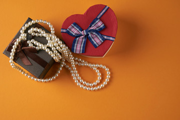 Pearl necklace with heart shaped gift box on a orange background, Love present card concept. Valentine's day theme