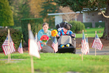 Father and disabled son in wheelchair visiting grave at cemetery