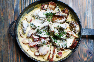 fried in a cast iron pan, sausage in a carrot-cream sauce with potatoes sprinkled with dill on the old wooden table. Flat lay.