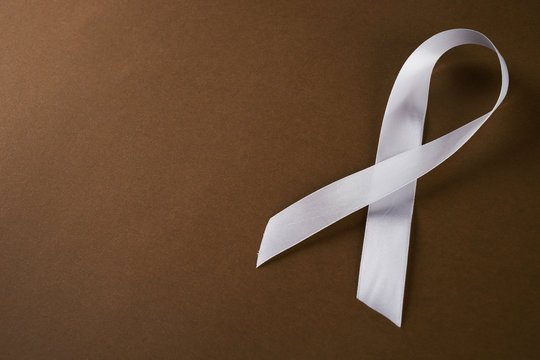 White awareness ribbon on brown background. Symbol of anti violence against women, safe motherhood. Top vew with copy spaced