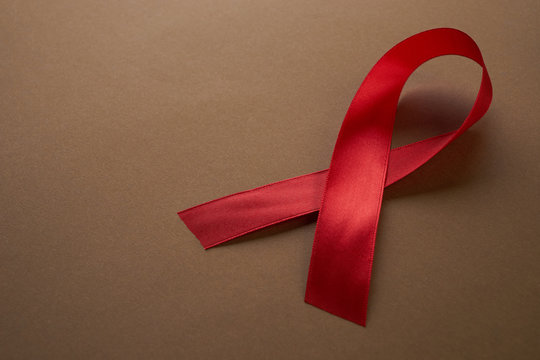 Red awareness ribbon on brown background. Symbol of solidarity with people living with HIV AIDS