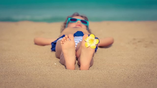 Child lying on the beach. Kid on summer vacation. Slow motion